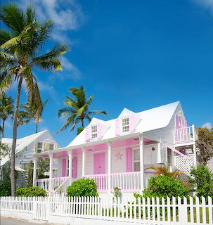 Pink cottage with white fence and palm trees under a blue sky