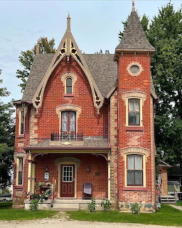Victorian red brick house with Gothic architectural details, pointed tower, and ornate wooden trim