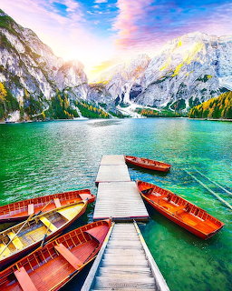 Wooden boats at a dock on a turquoise alpine lake with Dolomite mountains and colorful sunset sky