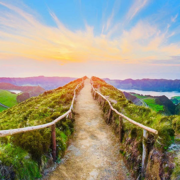 Wooden boardwalk path through green hills at sunset with dramatic sky and light rays