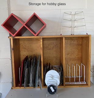 Wooden cabinet with slots storing stained glass sheets in various colors, red organizers and white rack above