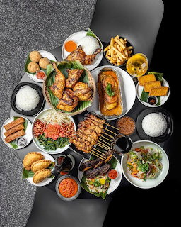 Overhead flatlay of various brunch dishes with grilled food, seafood, eggs, bread, and colorful sides on dark table