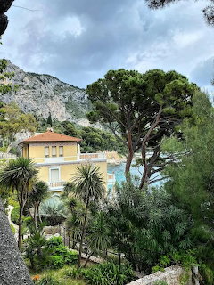 Yellow villa among green trees with turquoise Mediterranean sea and rocky mountain cliffs in background