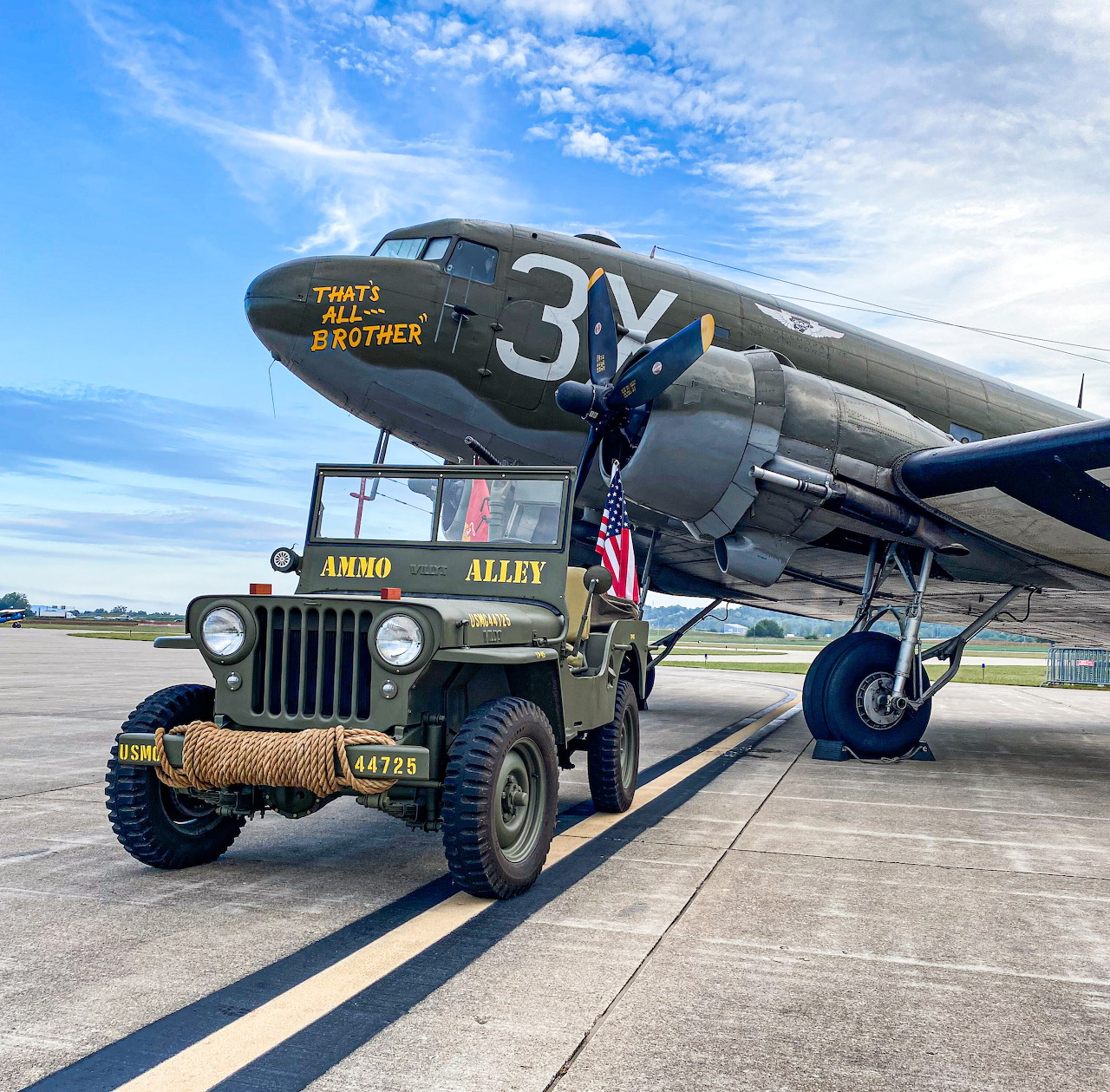 Olive drab 1946 Willys CJ-2A jeep with American flag next to vintage military transport plane on airfield