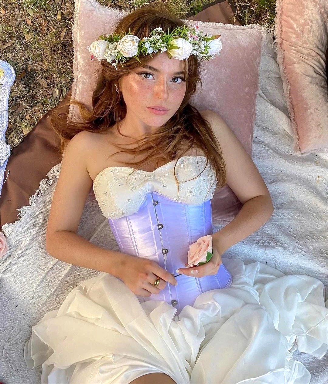 Woman lying on pillows in a white dress, lavender corset, and flower crown
