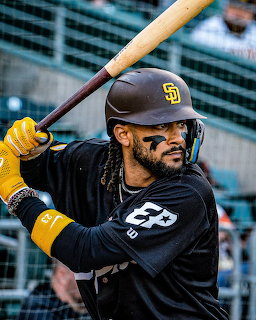 Fernando Tatis Jr in Padres black jersey holding a baseball bat in batting stance with yellow gloves