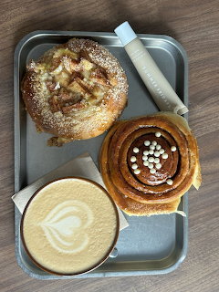 Top-down latte with leaf art and two pastries on a metal tray on a wooden table