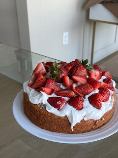 Round cake with whipped cream and sliced strawberries on a white plate