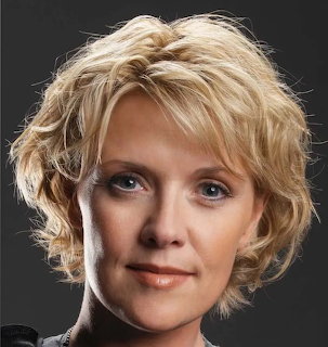 Close-up portrait of a blonde woman with short wavy hair against a dark background