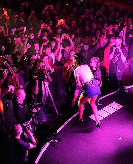 Female singer performing on stage with crowd holding phones in purple concert lighting