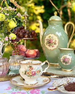 Vintage floral porcelain tea set with green teapot, teacup, vase, fruits, and flowers in a garden setting