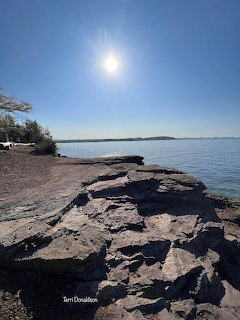 Sun over a calm lake with a rocky shoreline and clear blue sky
