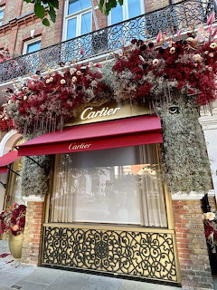 Brick storefront with red awnings and a large pink, red, and white floral display above the entrance