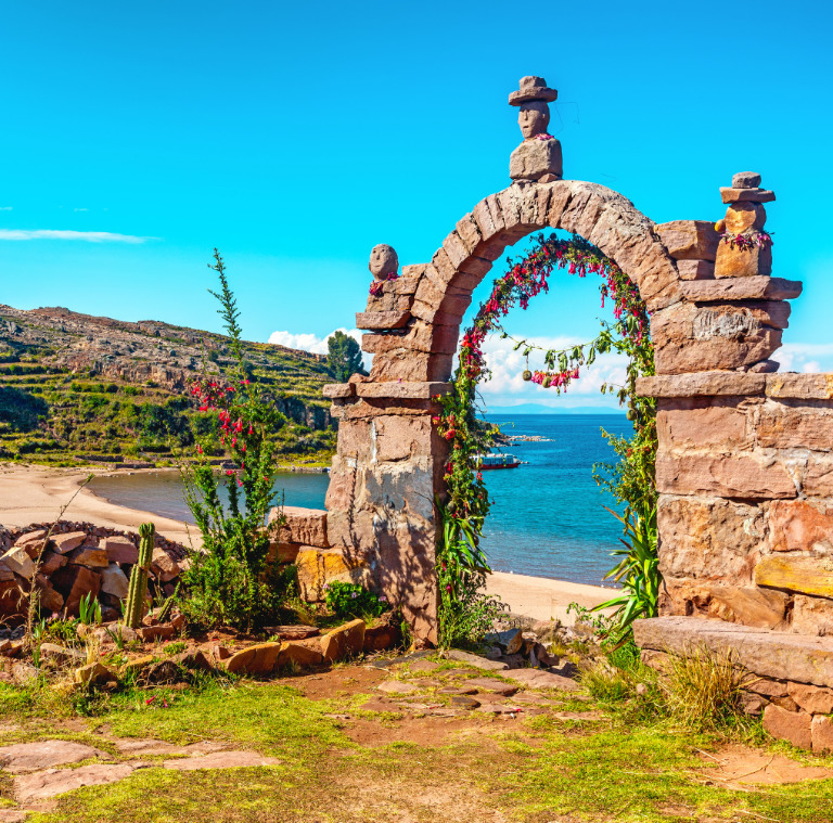 Stone arch by a lakeshore on Taquile Island, Peru, with blue water, hills, and clear sky