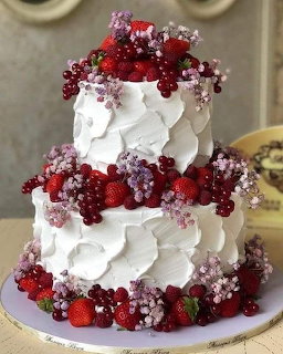 Two-tier white frosted cake topped with fresh berries and white flowers