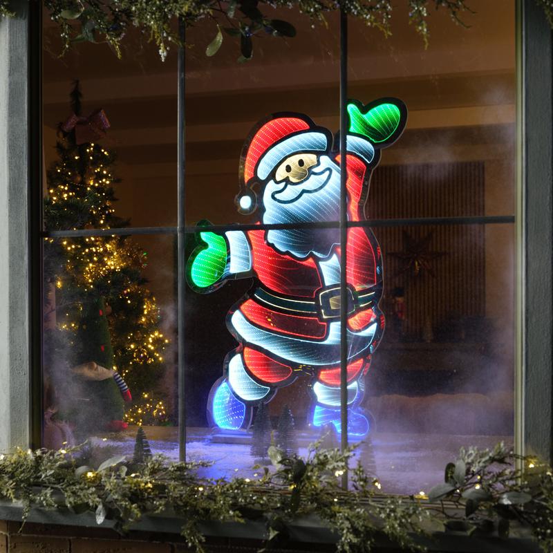 Illuminated Santa Claus decoration in a window with a Christmas tree in the background