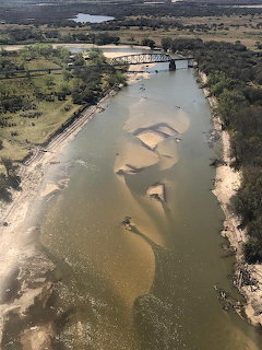 Aerial view of a river with sandbars, trees along the banks, and a bridge upstream.