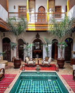 Moroccan riad courtyard with turquoise pool, arched colonnade, wooden balcony, and palm trees