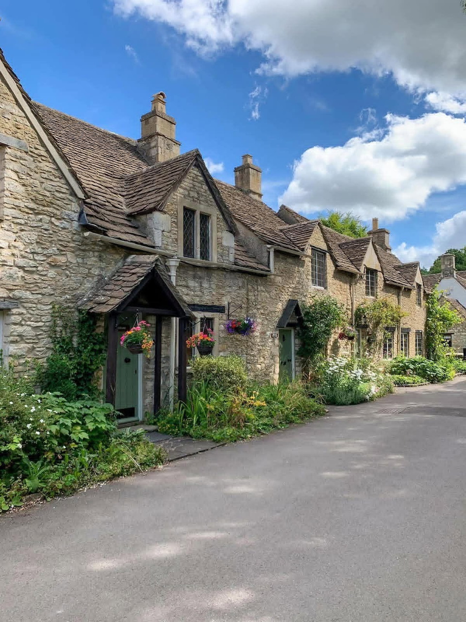 Stone cottages along a quiet road in Castle Combe village under a blue cloudy sky