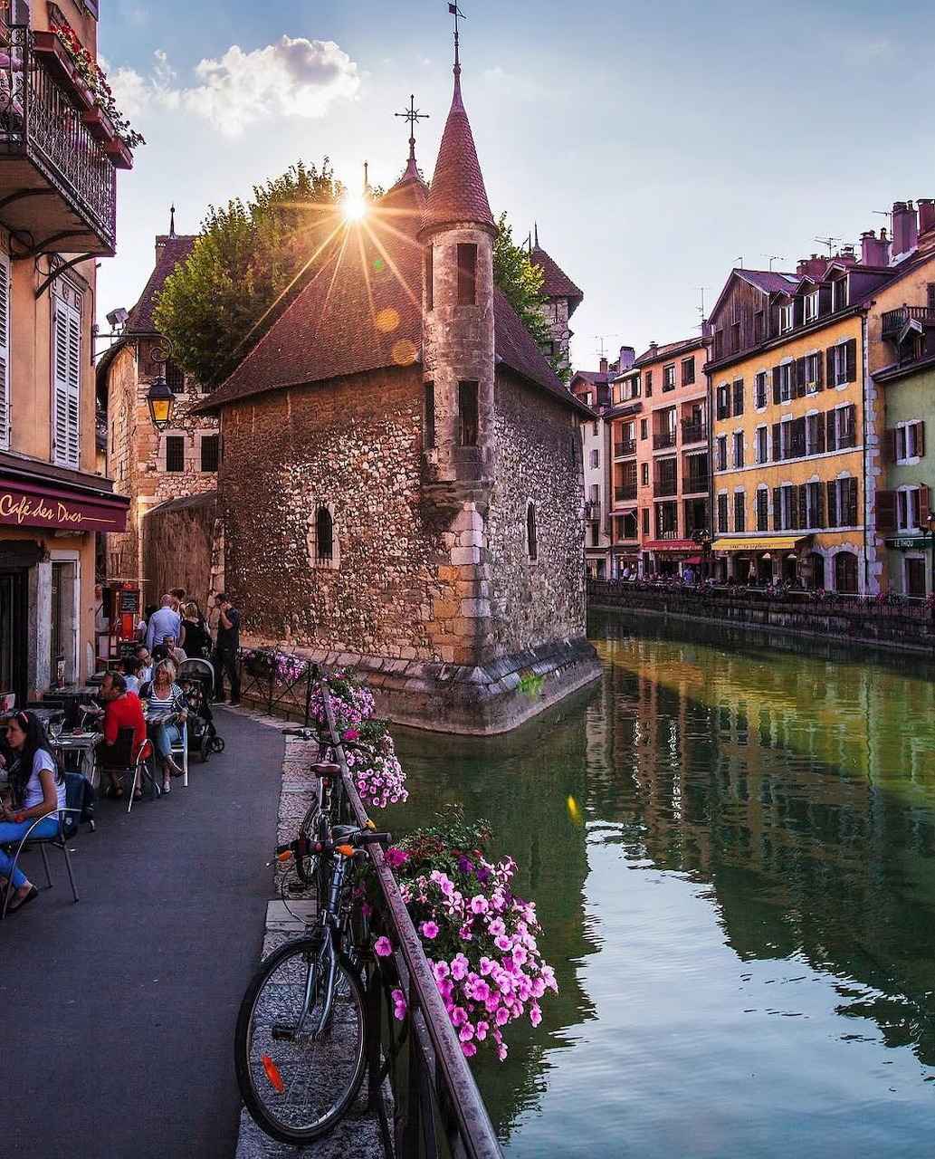 Old stone building beside a canal in Annecy with colorful buildings, flowers and a bicycle at sunset