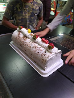 White frosted roll cake topped with strawberries and whipped cream on a tray