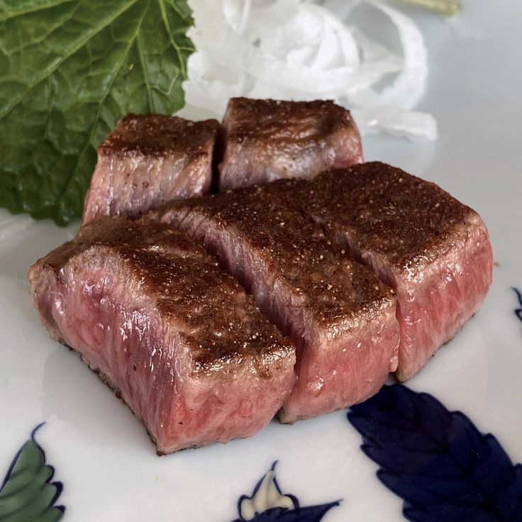 Sliced seared beef steak on a white plate with a green leaf garnish