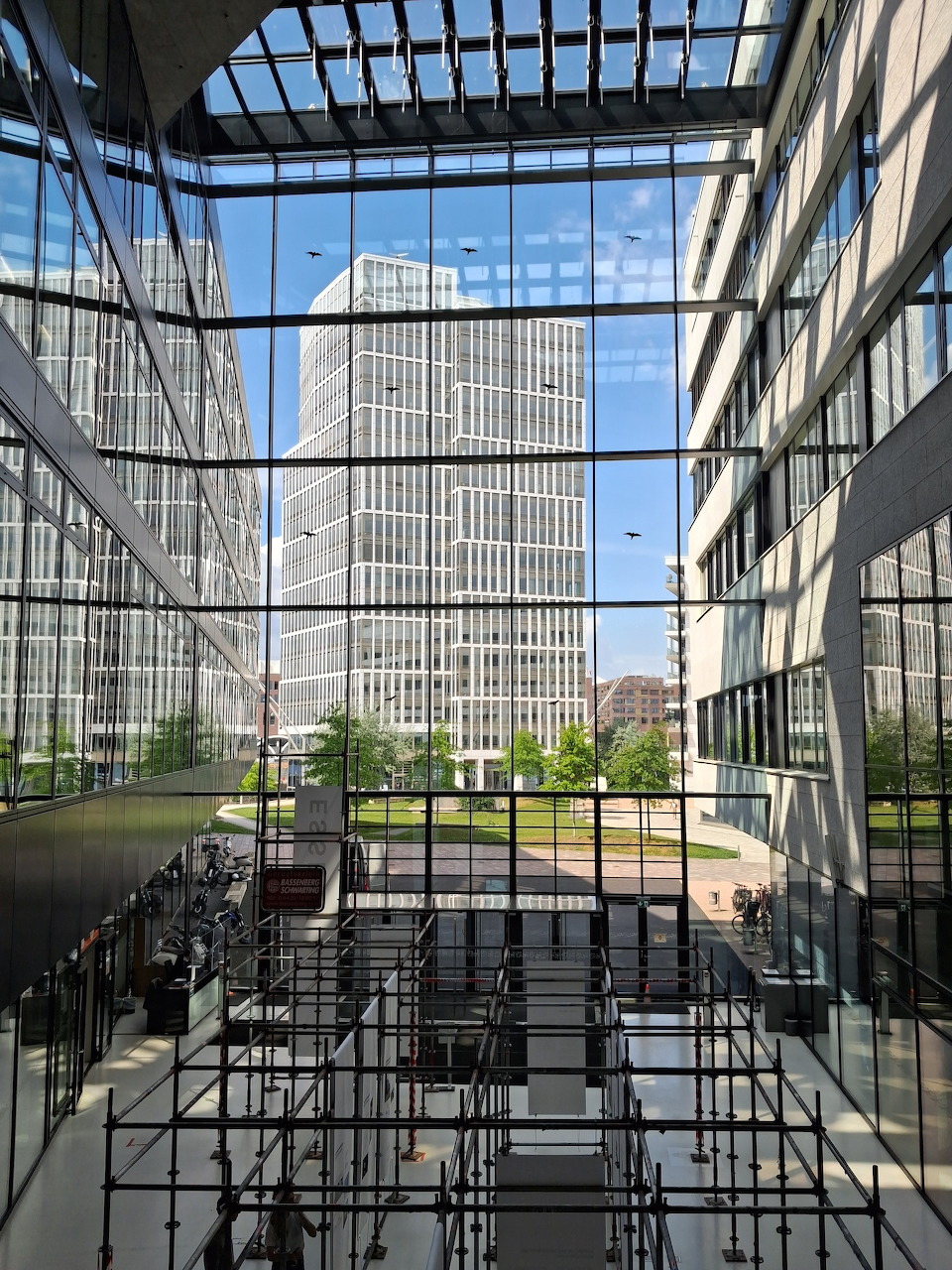 View through glass atrium toward modern Hamburg HafenCity buildings with green courtyard