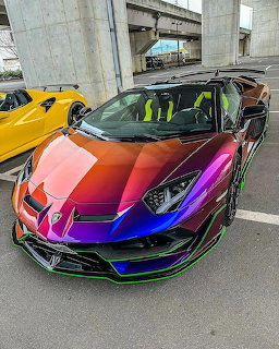 Rainbow chrome Lamborghini Aventador sports car parked under highway overpass with yellow car in background