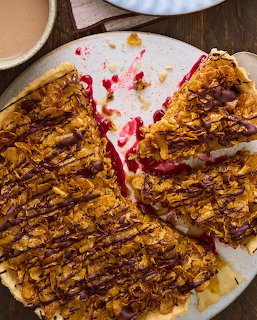 Sliced tart with caramelized almond topping and raspberry filling, one piece served on white plate