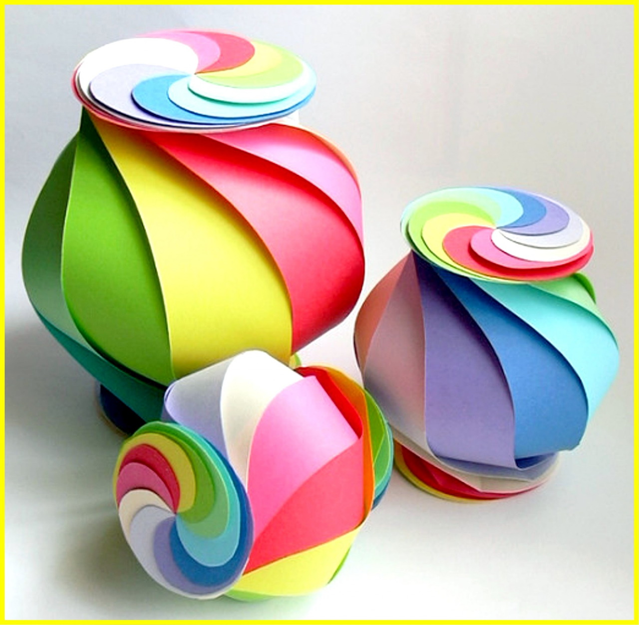 Three multicolored origami paper spheres with rainbow spiral patterns in different sizes