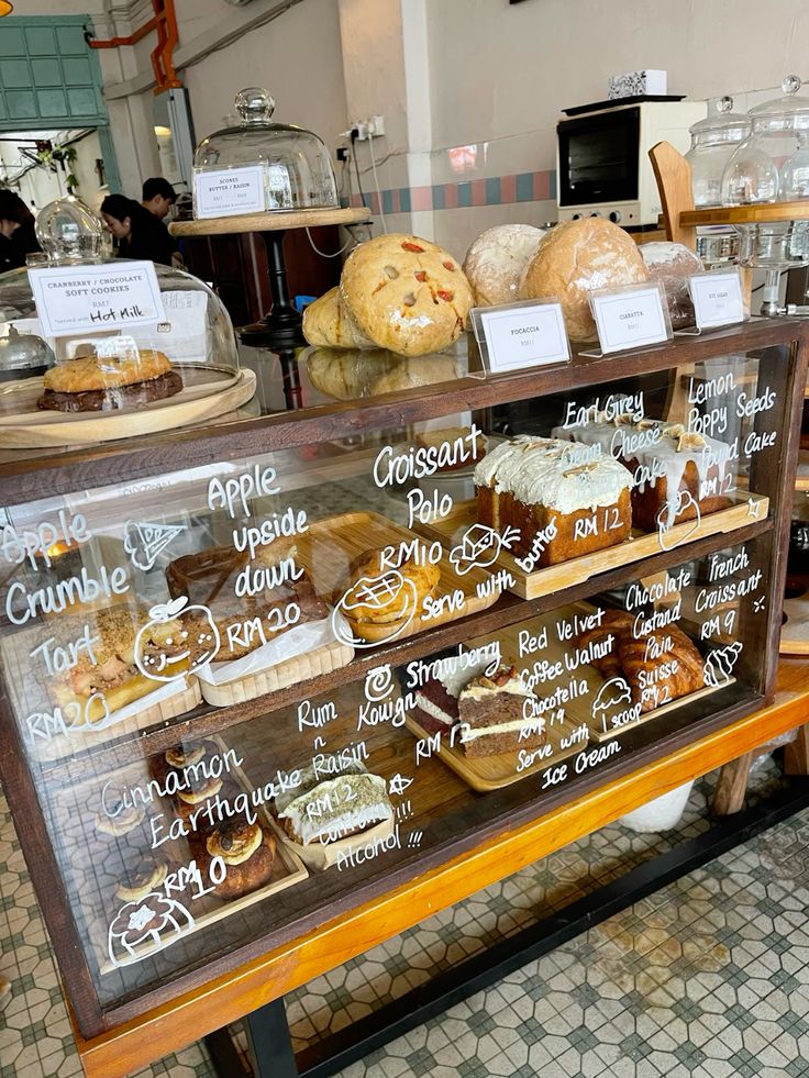 Wooden bakery display case with assorted pastries, bread, and cakes with handwritten chalkboard menu labels