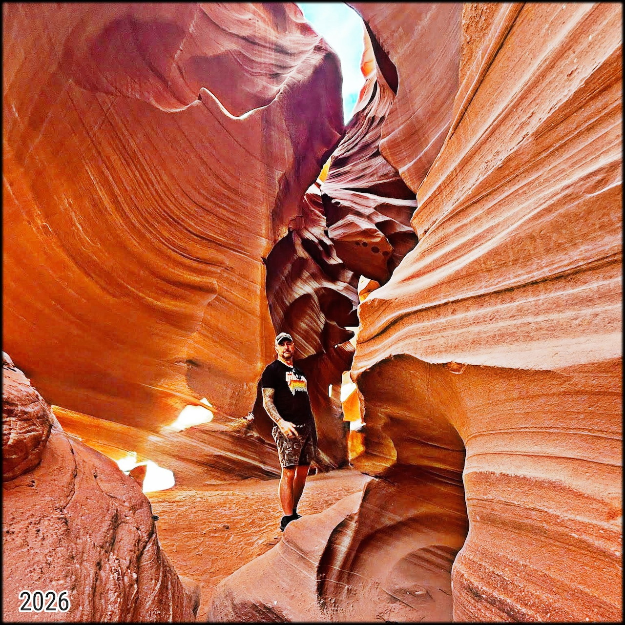 Person standing in narrow slot canyon with curved orange and red sandstone walls showing natural wave patterns