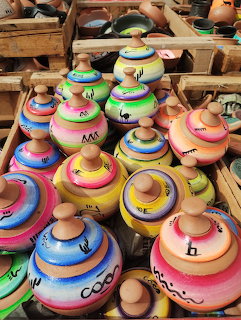 Rows of hand-painted clay pots with colorful striped patterns in yellow, orange, pink, blue, and green at a craft market