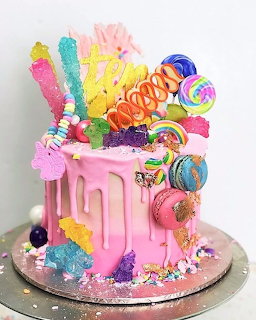 Pink frosted cake decorated with rainbow lollipops, candy sticks, marshmallows, and colorful confections on top