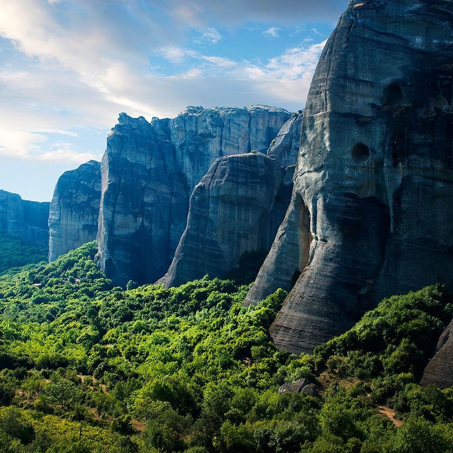 Towering gray rock formations of Meteora with dense green forest below and blue sky above