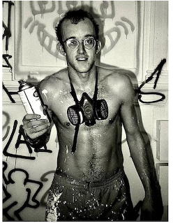 Black-and-white portrait of Keith Haring shirtless with glasses and a respirator around his neck