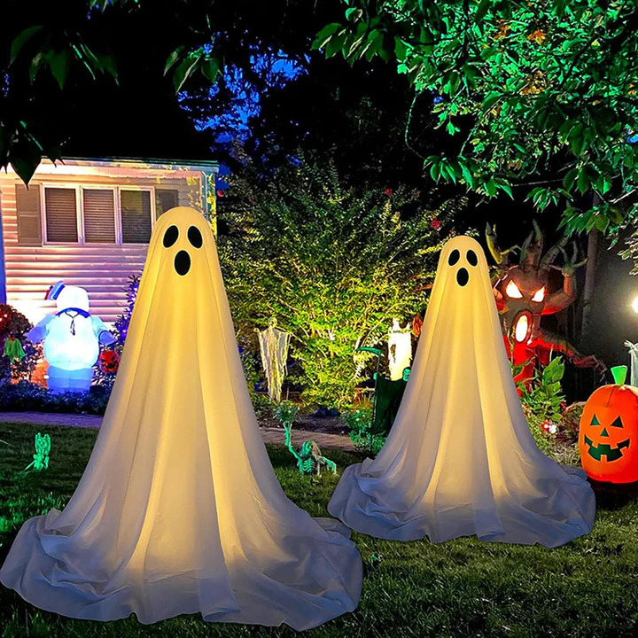 Nighttime Halloween yard with two large illuminated ghost decorations, pumpkins, and colorful outdoor lights