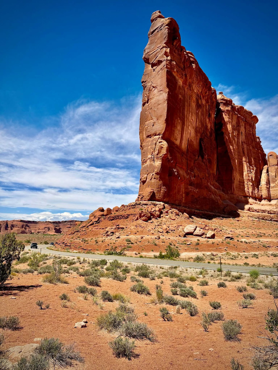 Tall red sandstone formation above a scrub-covered desert under a blue sky in Utah.