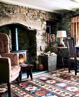 Cozy rustic living room with wood stove in stone fireplace, kilim rugs, and armchair