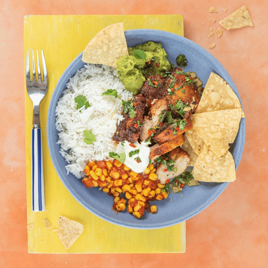 Overhead view of Mexican rice bowl with chicken, beans, guacamole and chips on blue plate