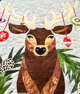Handmade quilt of a reindeer with Christmas ornaments hanging from its antlers and pine decorations