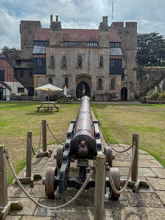 Historic cannon pointing toward Caldicot Castle entrance with cloudy sky and green lawn