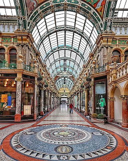 Ornate indoor shopping arcade with glass roof, mosaic floor, and symmetrical storefronts