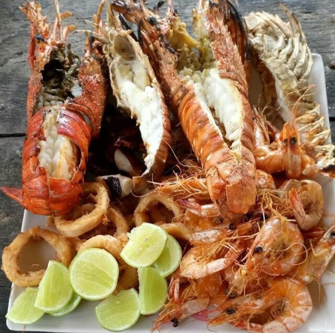 Grilled lobster tails and shrimp arranged on white plate with lime wedges and crispy onions