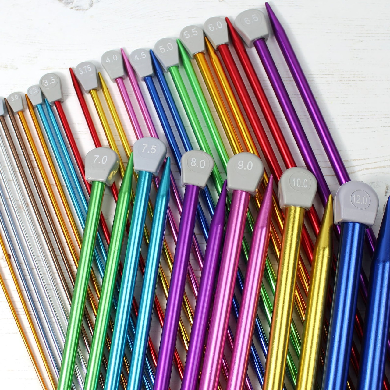 Close-up of colorful metal knitting needles fanned out on a white background