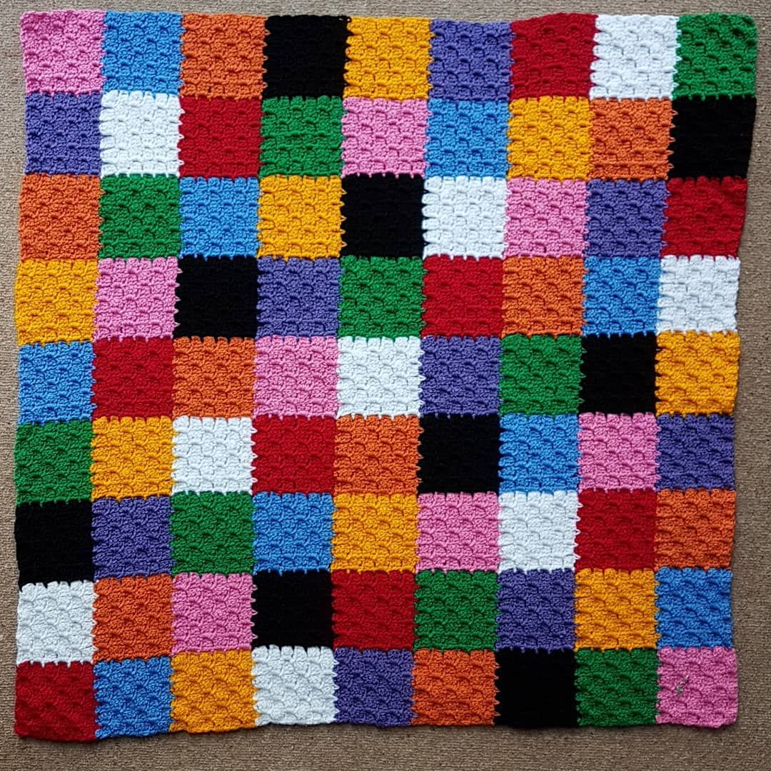 Colorful patchwork rug with grid of multicolored squares on wooden floor