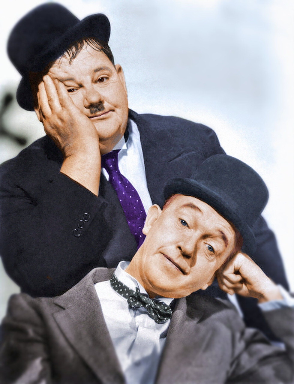 Laurel and Hardy in bowler hats, both resting faces on hands, smiling at camera in vintage portrait