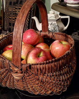 Wicker basket full of red and yellow apples on a table with dark woven fabric in the background