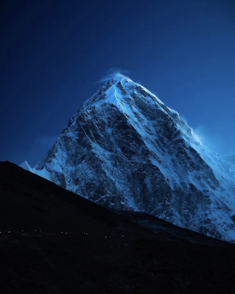 Snow-covered mountain peak glowing under starry blue night sky