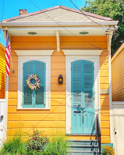 Small yellow house with turquoise door, shutters, wreath and American flag on front exterior